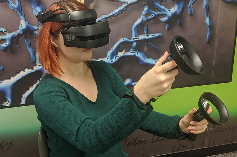 Woman wearing virtual reality headset and using handheld controllers.